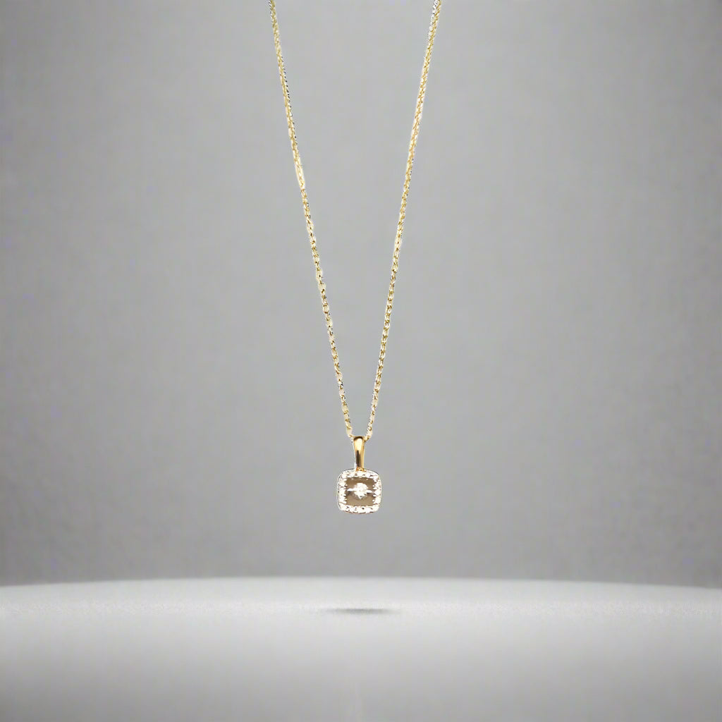 Gold necklace with a diamond pendant on a light gray background