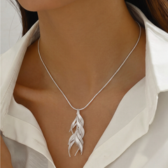 A close-up of a model wearing a delicate silver chain necklace with a silver leaf pendant, styled with a white collared shirt.