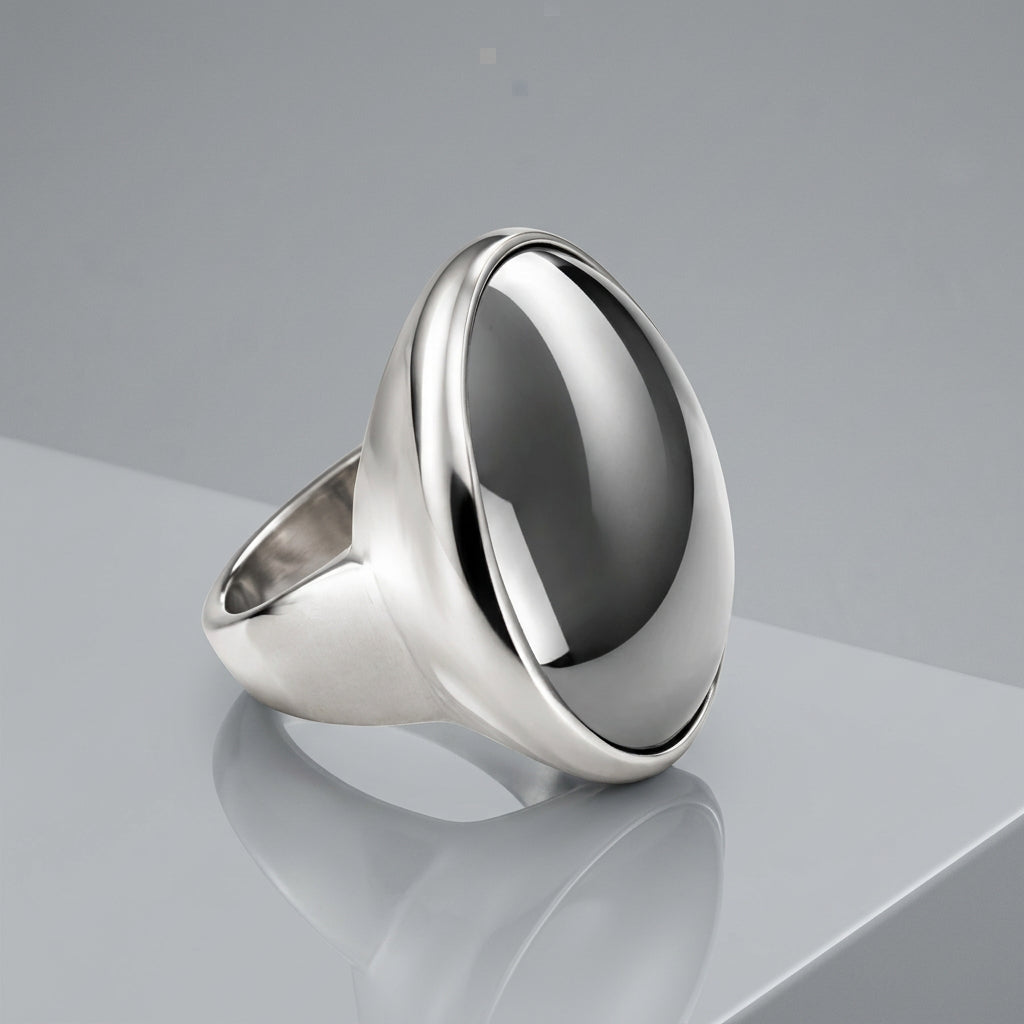A silver signet ring featuring a large, polished round cabochon gemstone with a dark gray center and bright silver edges, set against a clean white background.