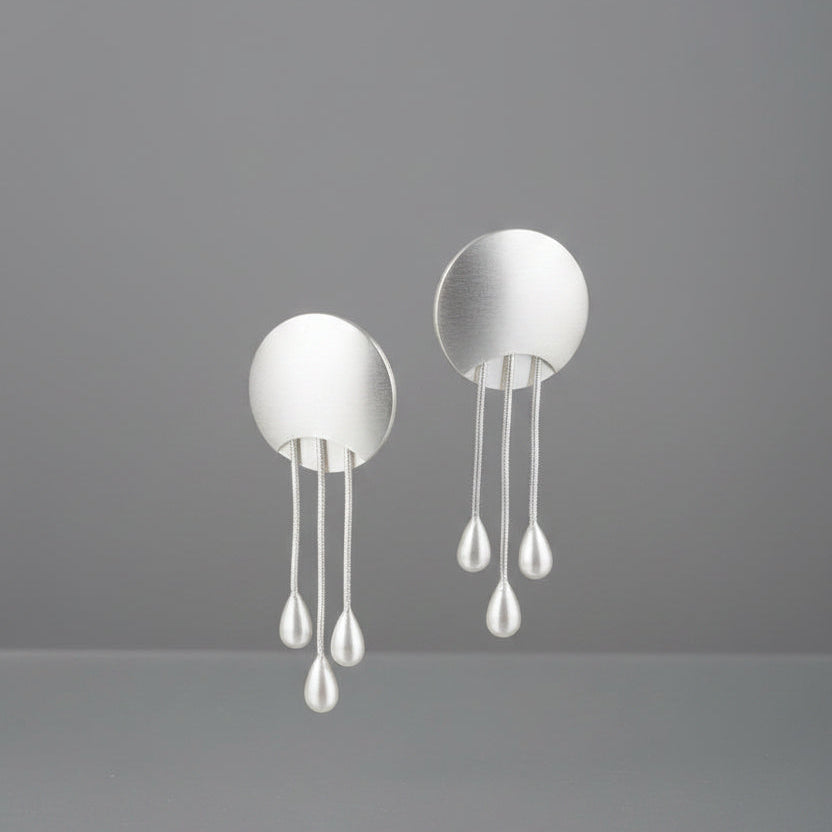 A pair of silver-toned dangle earrings with oval backings and three hanging pearl-like drops each.