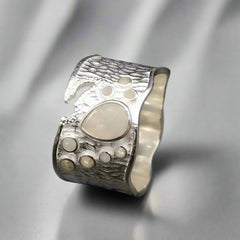 Silver ring with textured design on a dark background