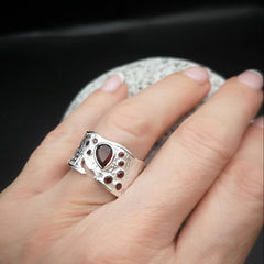 Silver ring with gemstones on a hand against a dark background