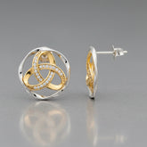 A pair of round interlocking knot stud earrings in yellow gold and white gold, with one earring shown from the front and the other from the side profile. The front earring features a central knot design paved with small clear stones, set within a double-ring circular frame.