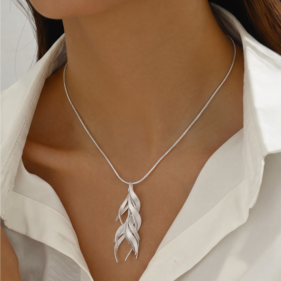 A close-up of a model wearing a delicate silver chain necklace with a silver leaf pendant, styled with a white collared shirt.