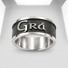 A silver-toned metal ring with a textured black center band featuring the engraved name 'Grá' in polished silver lettering, shown on a clean white background.