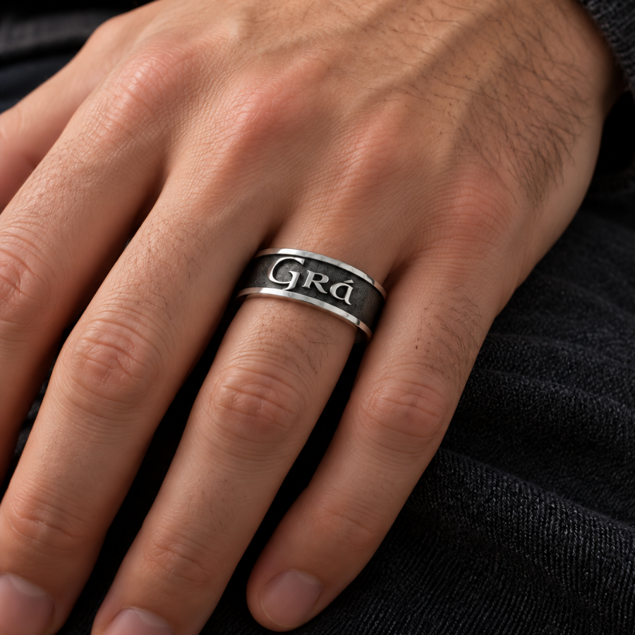 A close-up of a person's hand wearing a silver band ring engraved with the word 'Grad' on a dark textured sweater.