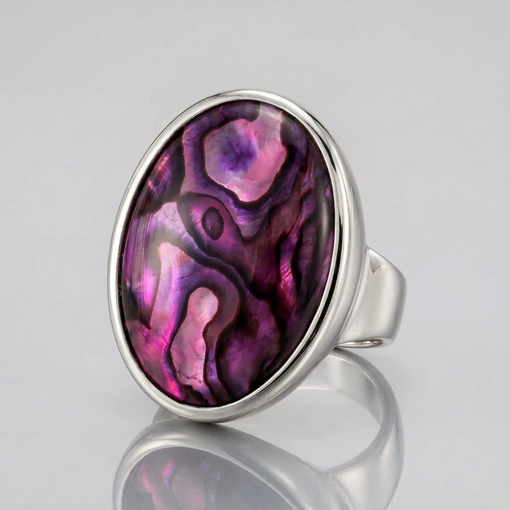 A silver-toned ring featuring a large oval bezel set with a vibrant purple and magenta abalone shell inlay, shown on a clean white background.
