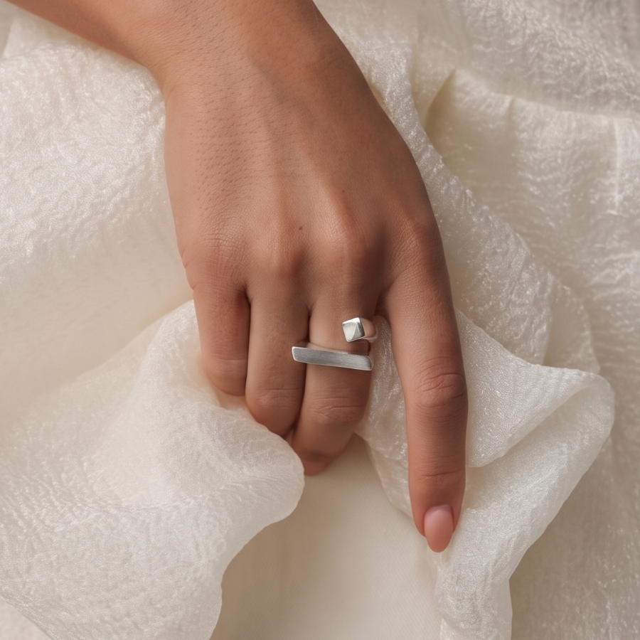 A close-up of a person's hand wearing a minimalist silver ring, resting on soft, textured off-white fabric.