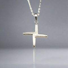 Silver cross pendant on a chain against a light background