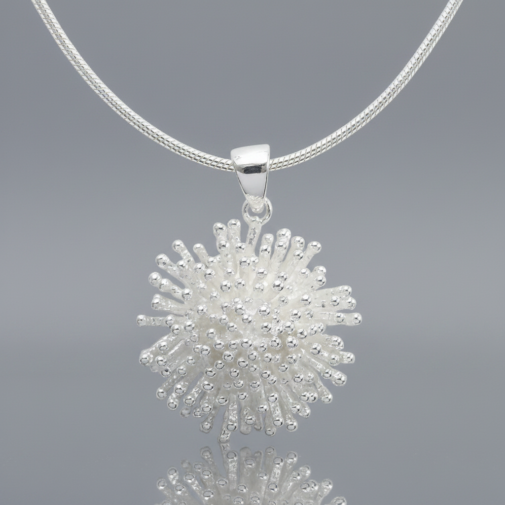 A silver pendant necklace featuring a textured,starburst like design on a matching silver snake chain, shown against a plain white background