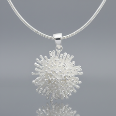 A silver pendant necklace featuring a textured,starburst like design on a matching silver snake chain, shown against a plain white background
