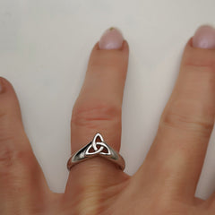 Silver ring with a Celtic knot design on a person's finger against a white background