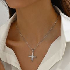 A close-up of a model wearing a silver cross pendant necklace on a delicate silver chain, styled with a white collared shirt.