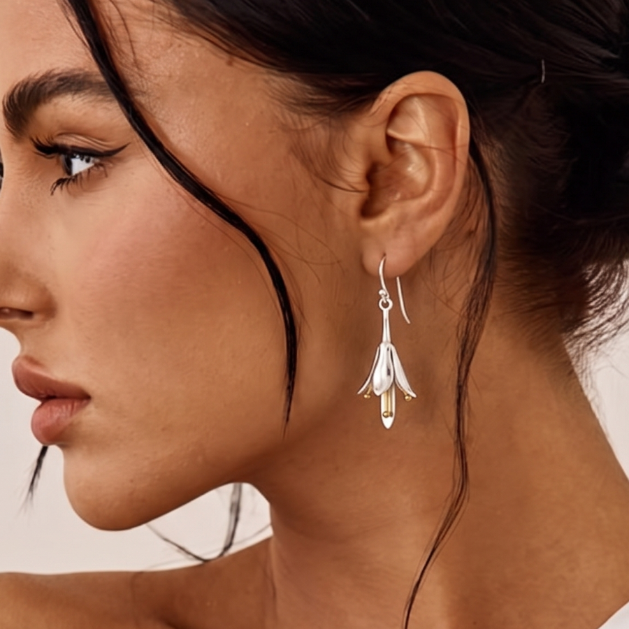 A close-up side profile of a woman wearing a delicate silver dangle earring with a floral or feather-like drop and small clear stones, against a soft light background.